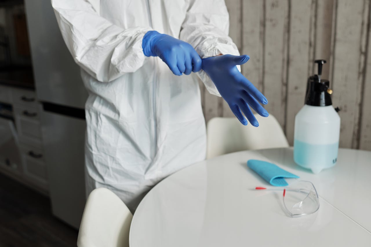 Individual wearing protective gear, preparing for cleaning with gloves and sanitizer.